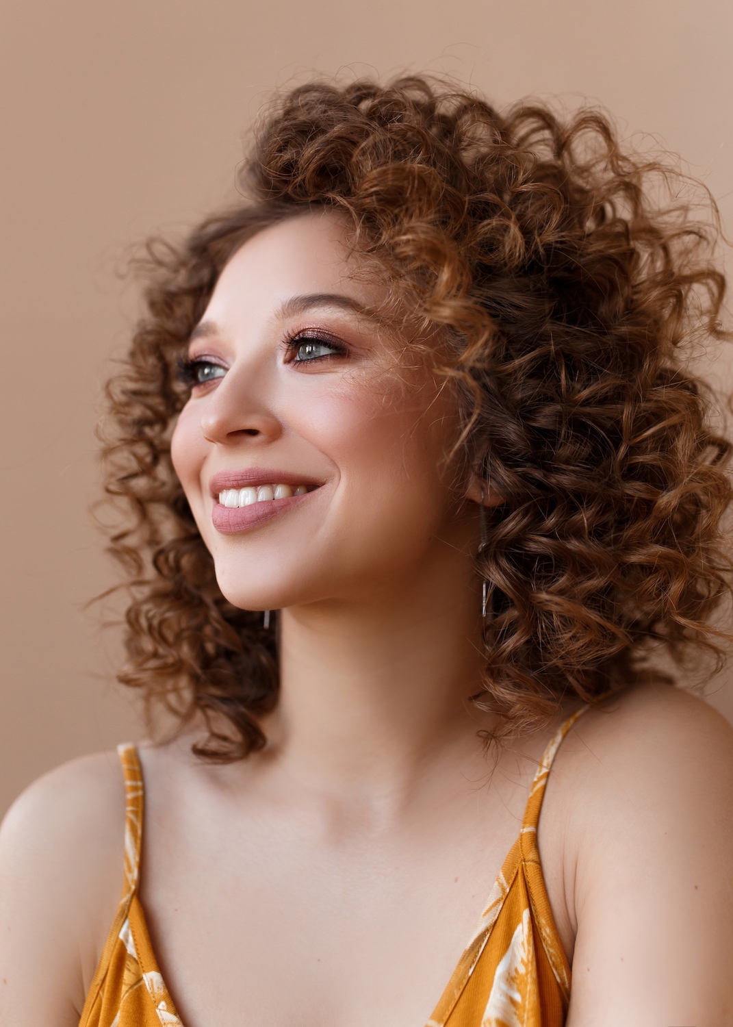 Smiling woman with curly hair and glowing skin, showcasing smooth complexion and natural radiance